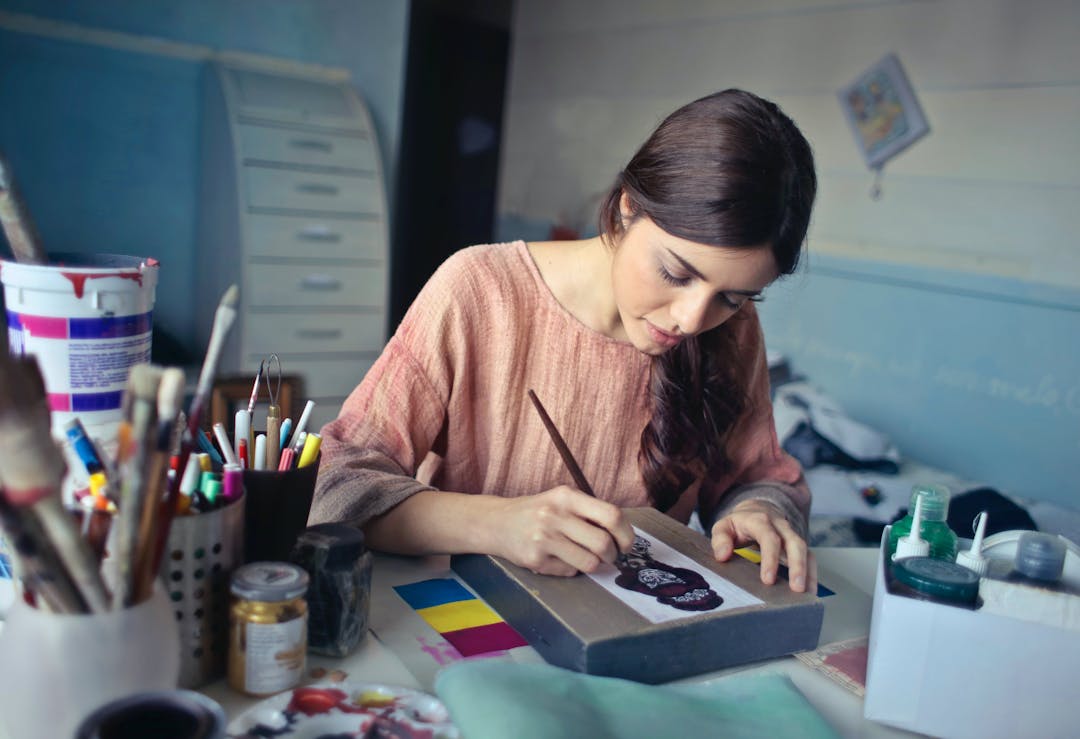 Focused woman painting on canvas among art supplies in a cozy studio space.