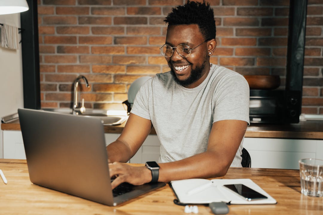 Cheerful man using a laptop in a modern kitchen with exposed brick walls.